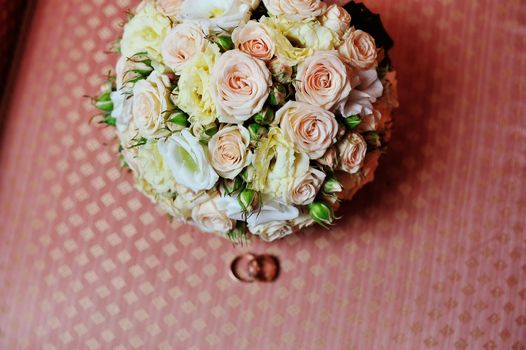 Pair of wedding rings and wedding bouquet on sofa.