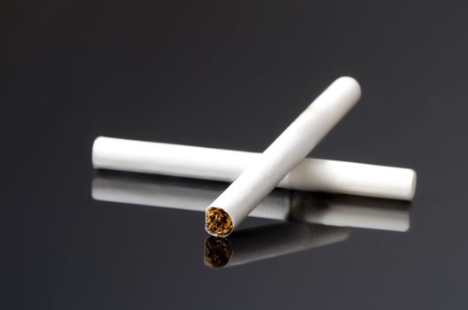 Two white cigarettes with reflection on black background. 