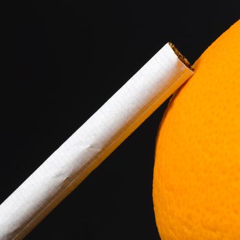 Lifestyle concept, cigarette and orange isolated on black background.
