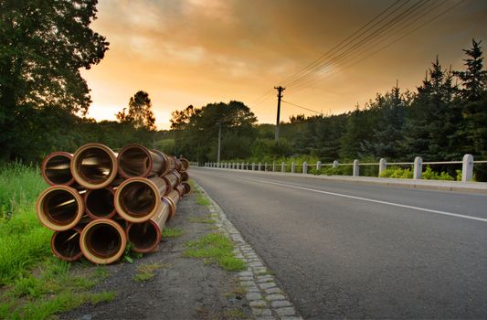 Road in the country, orange sunset sky and stack of pipes.