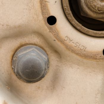 Detail of grey screw and iron car wheel. 