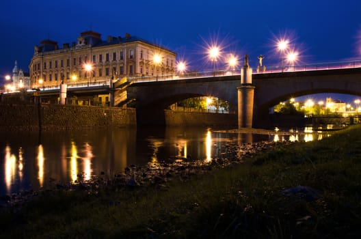 Panorama of bridge, river and school with lights at night. 