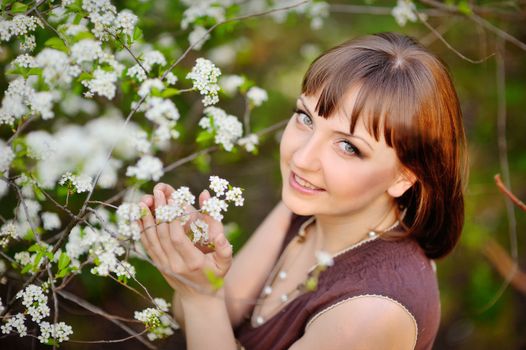 outdoor portrait of a beautiful brunette woman in blue dress among blossom apple trees 