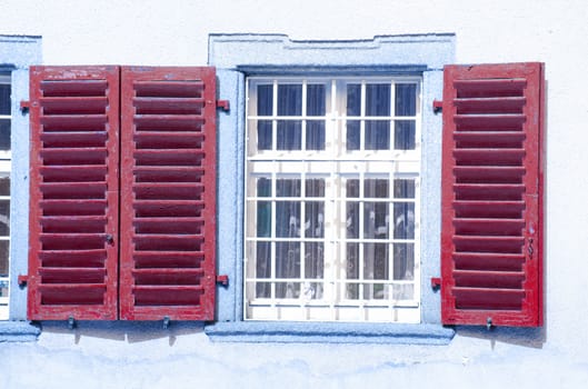 Blue house's facade and two windows with red shutters. 