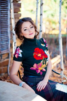 Pretty girl in black dress with flower sits near the house.