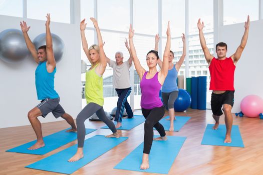 Full length of fit men and women exercising with hands raised at fitness club