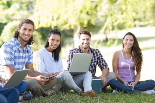 Smiling friends using media devices in park on a sunny day