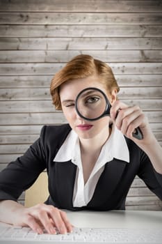 Redhead businesswoman looking through magnifying glass against wooden planks background