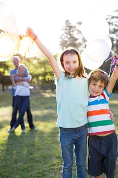 Happy siblings holding balloons at the park on a sunny day 