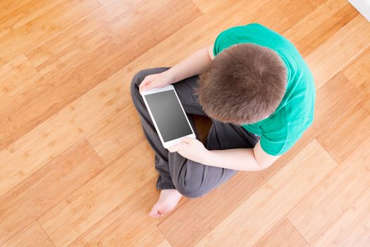 Male Kid Sitting on the Wooden Floor Holding his Tablet Computer From a High Angle View