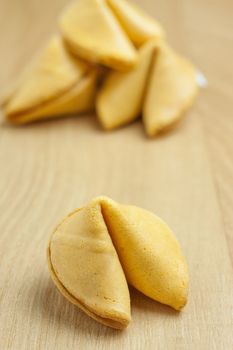 A fortune cookie with a pile of additional cookines in the background sitting on a wooden table.