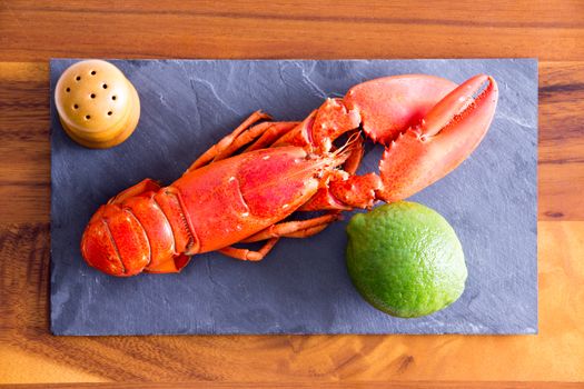 Close up High Angle Shot of Cooked Red Lobster on a Gray Cutting Board with Lime and Salt on Top of a Wooden Table.