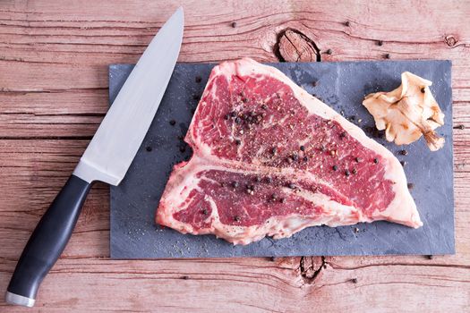 High Angle Shot of a Raw Pork Meat on a Cutting Board with Pepper, Golden Oak Shiitake Mushroom and Knife, Prepared on Top of the Wooden Table.