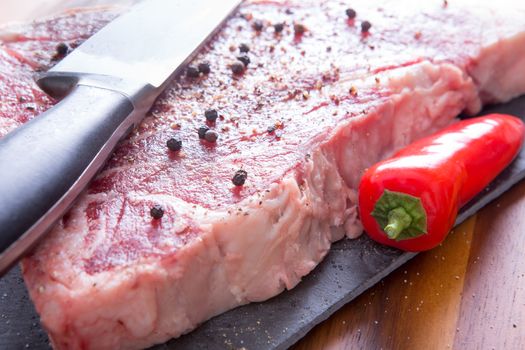 Close up Marinated Steak Meat with Whole Black Peppercorn on Top of a Cutting Board with Red Pepper and Knife