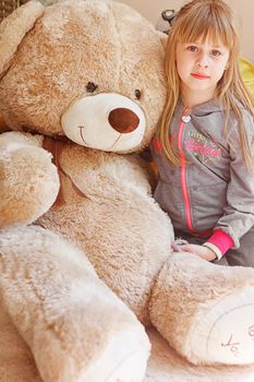 little girl hugging big teddy bear while sitting on chair