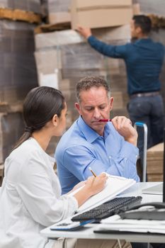 Warehouse manager writing on clipboard in a large warehouse