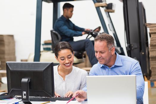 Warehouse managers working with laptop at desk in a large warehouse