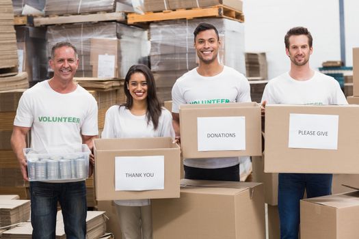 Volunteers smiling at camera holding donations boxes in a large warehouse