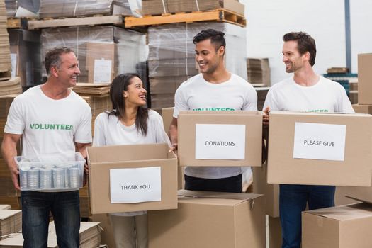 Happy team of volunteers holding donations boxes in a large warehouse