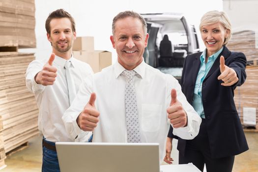 Warehouse team smiling at camera showing thumbs up in a large warehouse