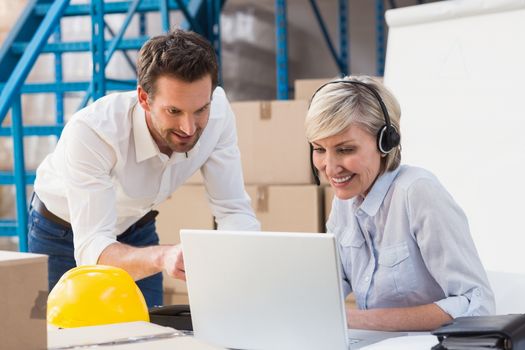 Warehouse managers using laptop and wearing headset in