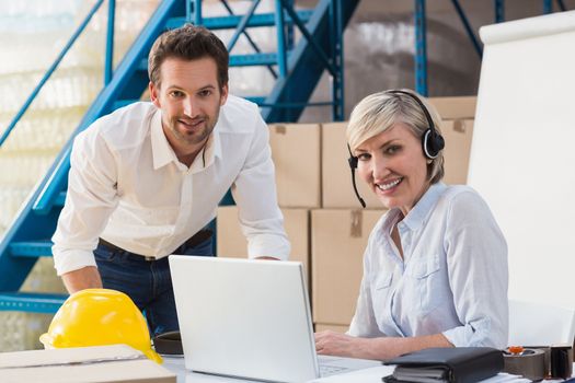 Warehouse managers using laptop and wearing headset in