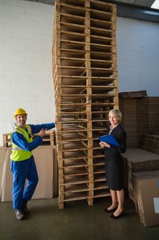 Worker and his manager in front of a stack of pallet in a large warehouse