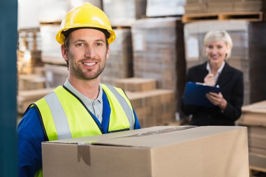 Warehouse worker holding box with manager behind him in a large warehouse