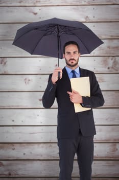 Serious businessman holding a file under umbrella against wooden planks