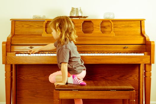 Right note requires effort outside your comfort zone in a conceptual image with a little girl climbing on the stool to stretch across a piano keyboard for the correct key or note