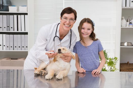 Smiling vet examining a dog with its owner in medical office