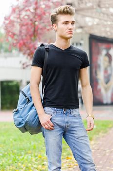 Attractive young man wearing black T-shirt and jeans with back pack standing outside