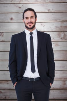 Smiling businessman in suit standing with hands in pockets against wooden planks