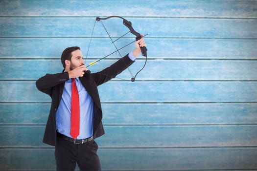 Focused businessman shooting a bow and arrow against wooden planks