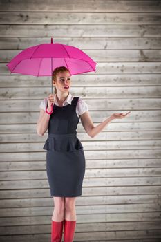 Pretty redhead businesswoman holding umbrella against wooden planks background