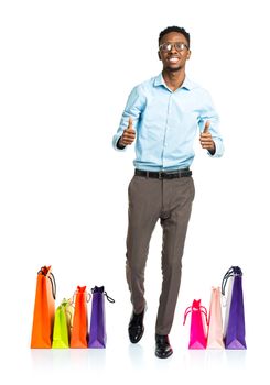 Happy african american man with thumbs up and shopping bags on white background. Holidays concept