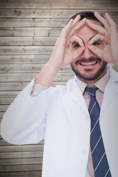 Smiling doctor forming eyeglasses with his hands against wooden planks background
