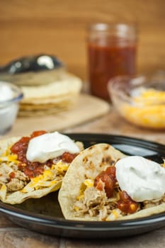 Pork carnitas with corn totillas on a dark plate with ingredients in the background.