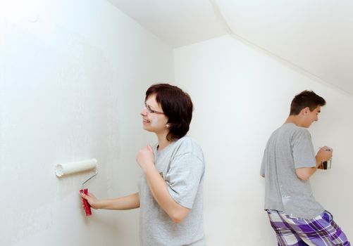 housewife with son painting wall in child room to white at home