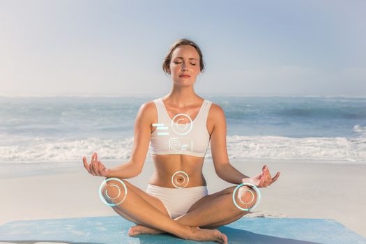 Fit woman sitting in lotus pose on the beach against fitness interface