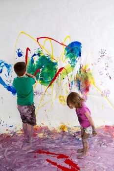 Young brother and sister painting together creating a modern abstract of vivid colors on the wall and floor using their imagination and creativity