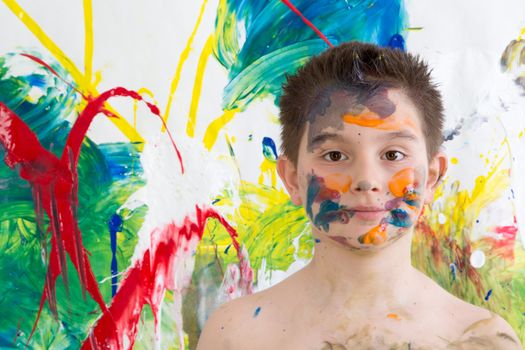 Young artist posing shirtless with his face covered in paint splodges with his modern art of colorful blended abstract patterns looking at the camera