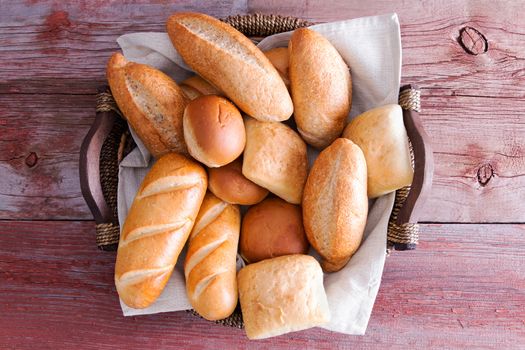 Assorted crusty fresh golden bread rolls in a basket in different speciality shapes displayed on a rustic wooden buffet table as an accompaniment to a meal