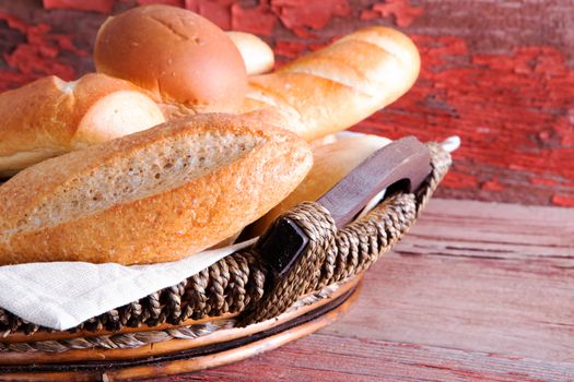 Basket of golden crusty fresh bread rolls in assorted shapes on a rustic wooden table ready to accompany dinner , close up side angle view