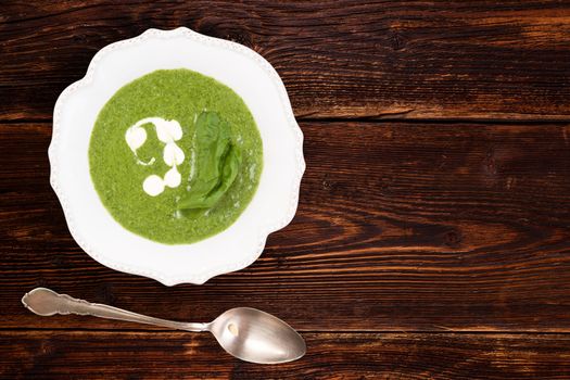 Spinach cream soup in rustic plate on wooden background, top view with copy space. Culinary soup eating. 