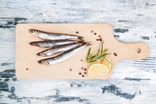 Delicious fresh sardines on wooden kitchen board with lemon, rosemary and colorful peppercorns on wooden background. Culinary healthy cooking.