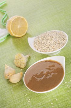 Tahini pasta in bowl, sesame seeds and lemon on green background. Culinary eating. 