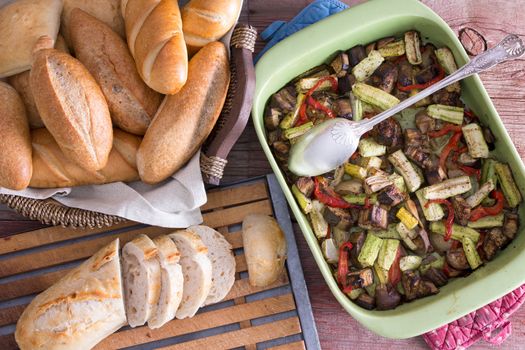 Healthy roasted fresh vegetables in an oven dish served with assorted crusty golden bread rolls and sliced baguette as a healthy snack or accompaniments to a meal