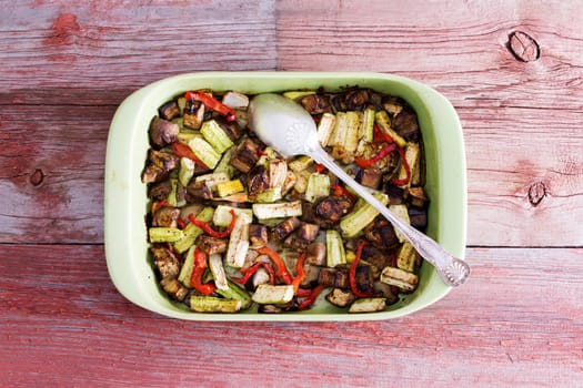 Delicious seasoned fresh roasted assorted diced vegetables in a serving dish with a silver spoon viewed from above on a wooden table or kitchen counter