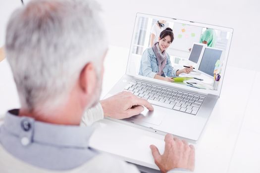 Closeup rear view of a grey haired man using laptop at desk against artist drawing something on graphic tablet with colleagues behind